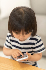 自宅の居間でスマートフォンを見る3歳の女の子