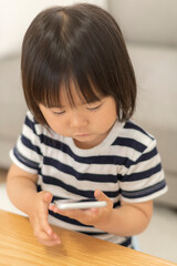 Naklejka premium 自宅の居間でスマートフォンを見る3歳の女の子