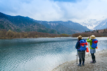 Fototapeta premium Hikers wearing colourful attire stop and photograph Lake Taisho and the distant snowy mountain peaks of Chubu Sangaku National Park in Kamikochi, Nagano Prefecture, Japan. Selective focus.