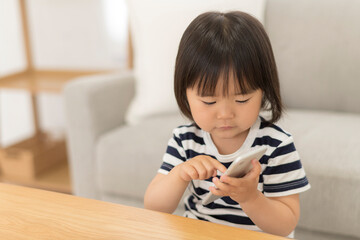 Naklejka premium 自宅の居間でスマートフォンを見る3歳の女の子