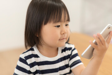 自宅の居間でスマートフォンを見る3歳の女の子