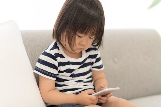 自宅の居間でスマートフォンを見る3歳の女の子