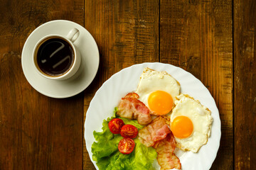 On a wooden table is a plate with fried eggs and a cup of coffee.