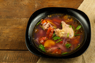 Black dish of vegetable soup on a tablecloth on a wooden table.