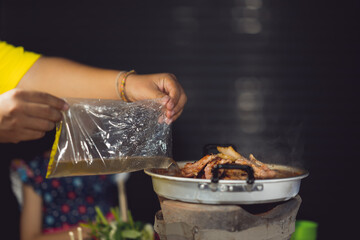 Grilled meat on pan and people use chopsticks for eating 