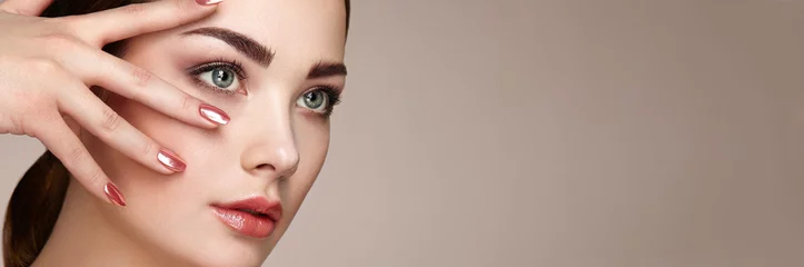 Foto auf Acrylglas Nagelstudio Schönheit Brunettefrau mit perfektem Make-up. Rote Lippen und Nägel. Perfekte Augenbrauen. Grundierung für die Hautpflege. Schönheitsmädchengesicht lokalisiert auf beige Hintergrund. Modefoto