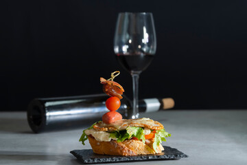 a delicious looking open sandwich with cheese and an assortment of meat and vegetables on a dark plate