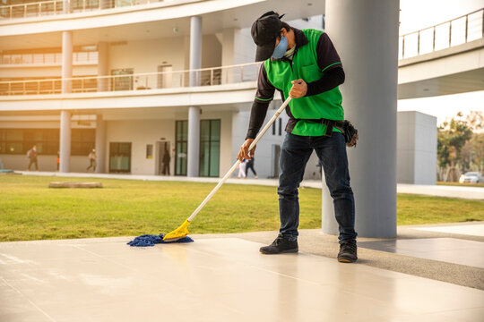 A Man Janitor  Wear Face Mask Cleaning Floor With Mopping  On Modern Building