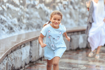 Happy beautiful girl running through the spray of water.