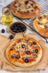 Pizza with olives on paper and wire rack on a gray background with a bottle of oil