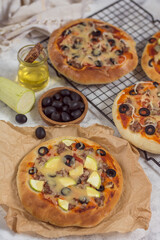Pizza with olives on paper and wire rack on a gray background with a bottle of oil vertical arrangement