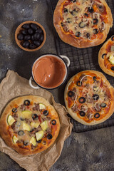 Pizza with olives on paper and wire rack on a dark background with a bottle of oil and sauce top view
