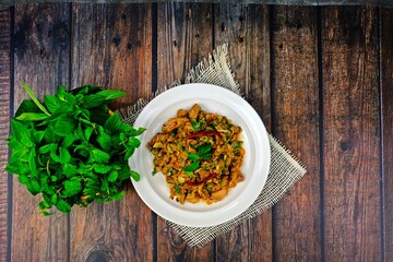 Hot and spicy grilled pork neck salad with peppermint leaves and Thai basil leaves on wooden table.