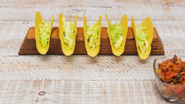 The process of making delicious hard shell tacos - with the filling ingredients in bowls marching through the screen and assembling the popular mexican dish - top view, stop motion animation