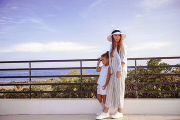 Mother and Sweet little  girl in beautiful dress, summer hat plays walks outdoors on warm sunny summer day.