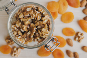 Raw walnut stored in glass food container and dried apricot and almond on wooden table