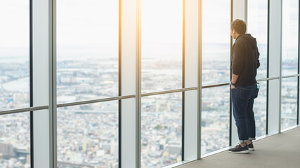 young Asian man standing and  looking out window glass on top of Umeda Sky Building at osaka Japan. - Powered by Adobe