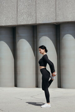 A distant shot of a girl practicing outdoors and stretching quadriceps on the outside of her thigh