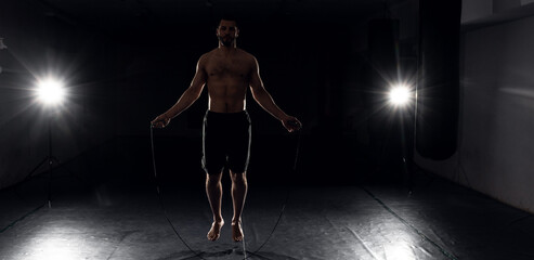 Fototapeta na wymiar boxer on a dark background flexes before training on a jump rope
