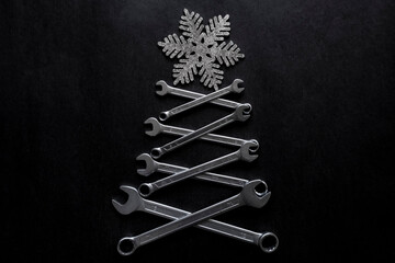 Abstract christmas tree made of wrenches with snowflake on the top on black background. Industrial...