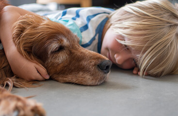 Young boy lying on the floor with big, old dog, boy hugs the dog