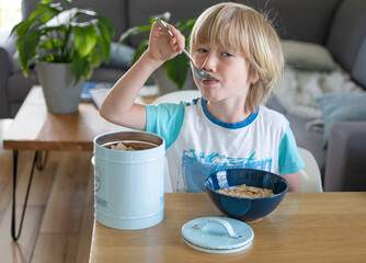 Boy eats cereals with milk, in dining room, at the table, in the background living room, sofa, coffee table
