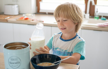 Boy makes cereals with milk, in the white kitchen, in the background window