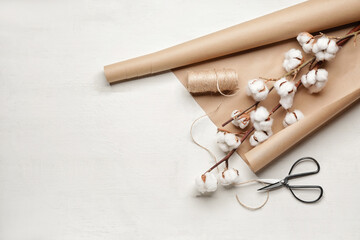 Beautiful cotton flowers, wrapping paper, thread and scissors on white background