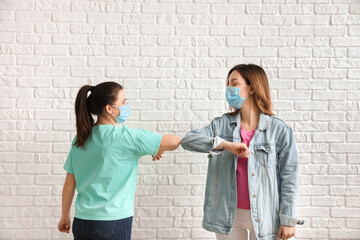 Young women greeting each other near brick wall. Concept of social distance during coronavirus...