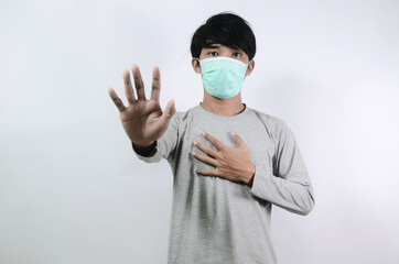 Asian man showing stop sign. Social distance concept. Asian man in a gray t-shirt and wearing a medical mask isolated on a white background