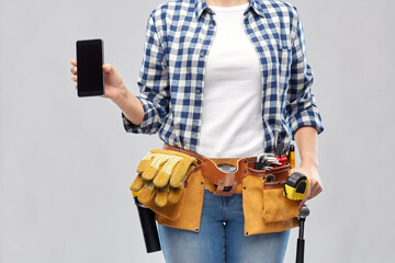 repair, construction and building concept - woman or builder with smartphone and working tools on belt over grey background