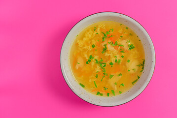 Vegetable clear soup with eggs served in a bowl isolated on bright pink background.