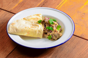 Meat with gravy and fresh greenery served with a piece of lavahs bread on white plate over dark rustic background.