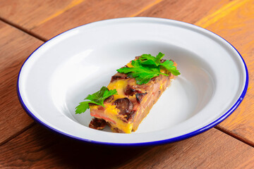 Homemade meat casserole with mushrooms and tomatoes and fresh pardley served on white plate over wooden background.