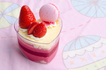Heart shaped red velvet cake decorated with strawberry and macaron on pink background