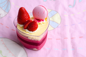 Heart shaped red velvet cake decorated with strawberry and macaron on pink background