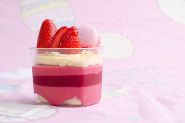Heart shaped red velvet cake decorated with strawberry and macaron on pink background