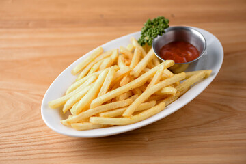 Golden French fries potatoes ready to be eaten. Served with tomato sauce on a white late over rustic wooden background.