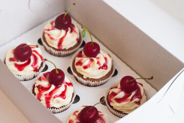 Vanilla cupcakes in gift box with berry sauce, whipped cream and fresh cherries on top.