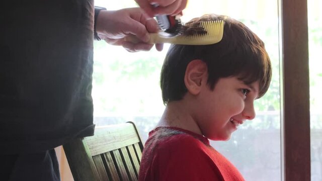 Hair cutting at home. Epidemic of coronavirus infection COVID-19. Hairdressers are closed.A serious child on a haircut by dad. A boy in red clothes is scissored by cutting bangs on his head.
