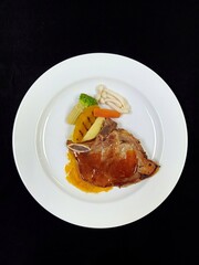 Pork chop in a white dish with vegetables decorated on a black background.