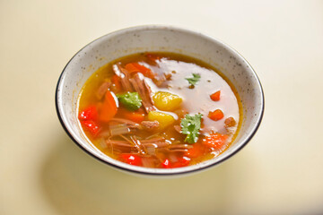 Delicious stew soup with meat and vegetables served in a white bowl over bright pastel yellow background. Healthy diet.