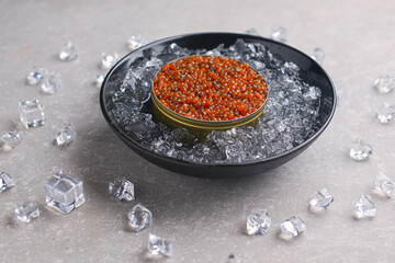 Bowl of red caviar on vintage black metal tray with ice over gray texture background. Top view,...