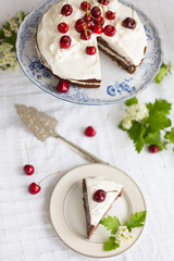 Piece of homemade cherry cake with whipping cream and cherry berry on top surrounded with flowering  branches on white tablecloth