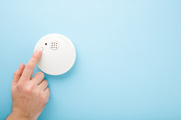 Young man finger touching new white plastic smoke alarm. Light blue table background. Pastel color....