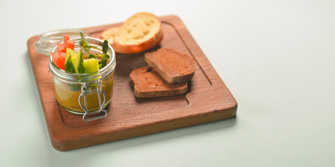 Fototapeta na wymiar Plate with fresh vegetables and thick sauce in a jar, with different kinds of bread, served on a rustic wooden board.