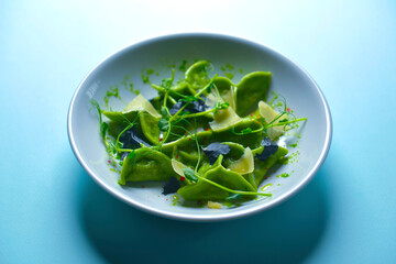 Green spinach ravioli dumplings with ricotta cheese and meat filling served in a blue plate over pastel blue background.