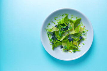 Green spinach ravioli dumplings with ricotta cheese and meat filling served in a blue plate over pastel blue background.