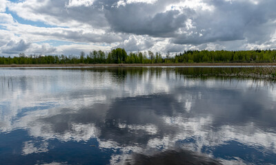 landscape with calm lake water, white cumulus clouds and reflections in the water
