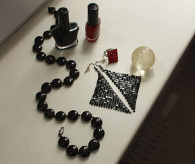 Black beads made of natural agate, nail polishes, shiny disco earrings, a transparent shiny ball, a red matrix ring, on a white windowsill.